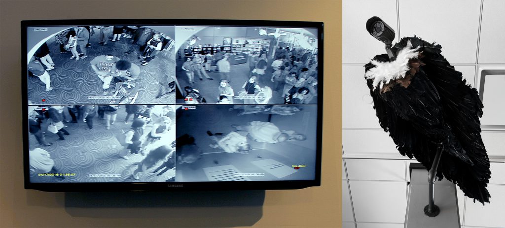 A monitor showing four frames of security camera footage. Next to it is a sculpture of a vulture with a security camera for a head.