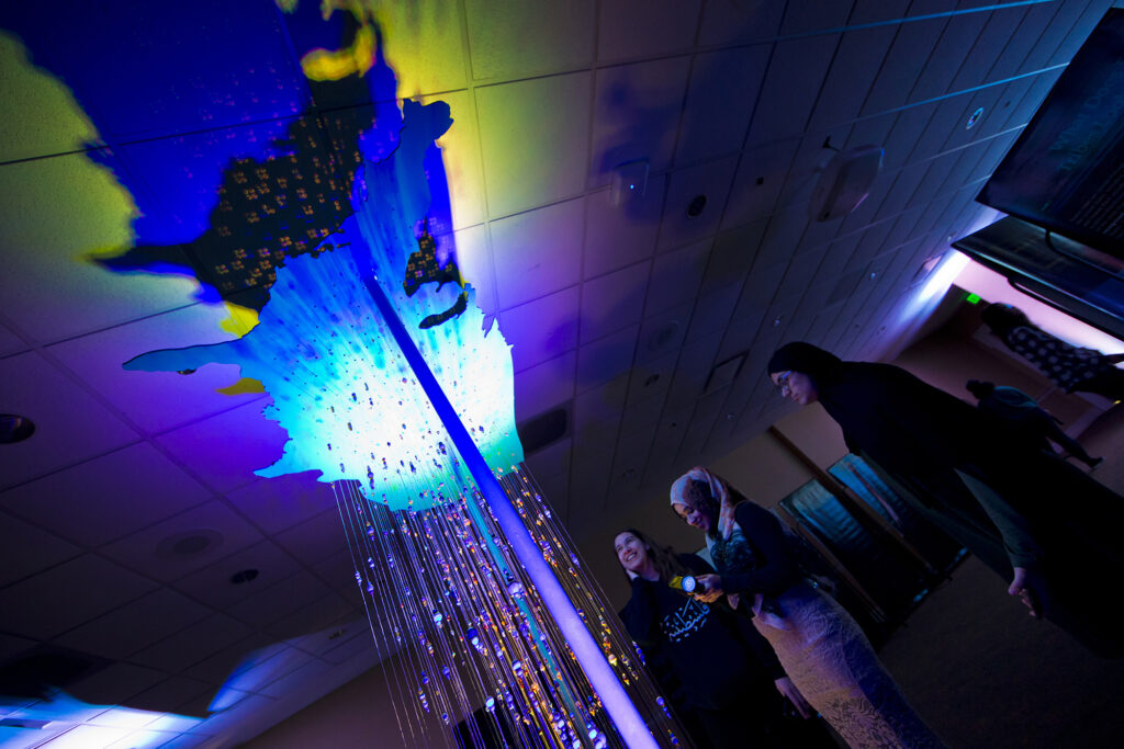 Students shine a blacklight on a beaded sculpture.